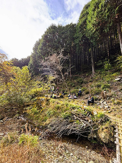 春嶽湧水付近の日当たりの良い斜面でお弁当を食べる参加者たち